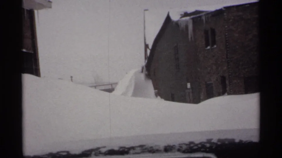 1971 Wisconsin 8mm frame with a brick building and streetlight partly hidden behind a high, rounded snowdrift.