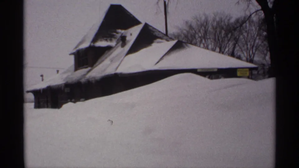 1971 Wisconsin winter frame showing a peaked-roof building, bare trees, and a broad foreground snowbank.