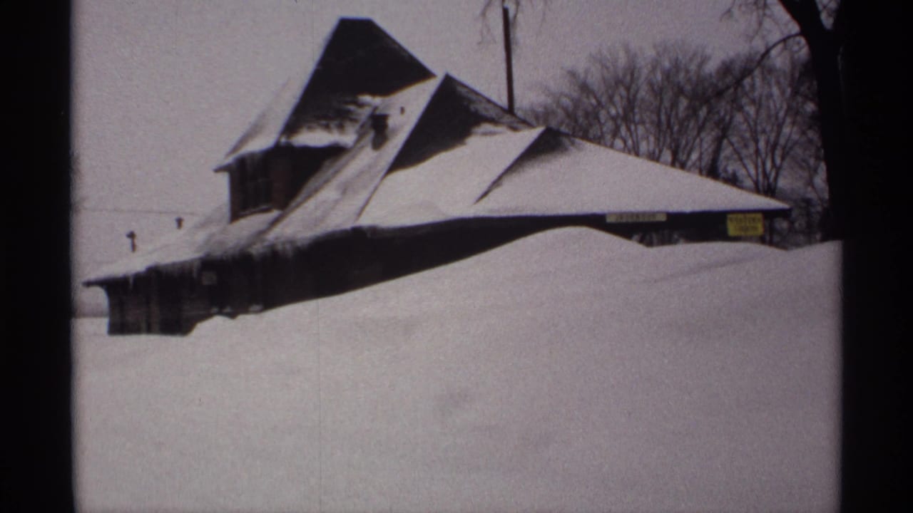 Snow-covered steep-roofed building nearly buried behind a high drift.
