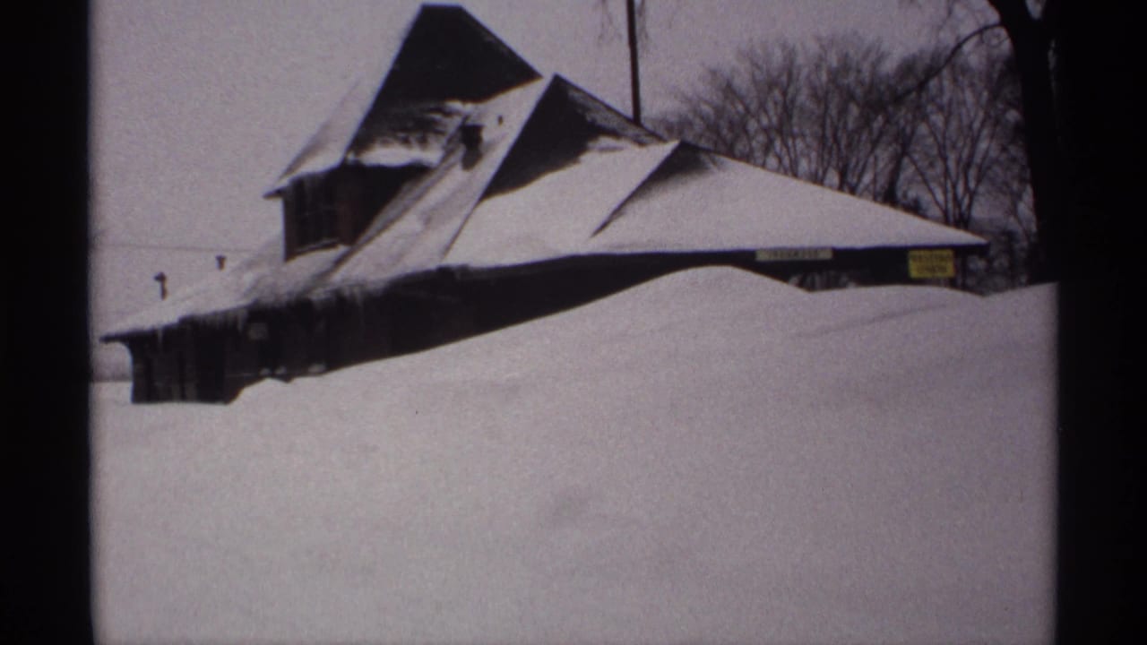 Snowbound building with angular roof and deep drift across the foreground.