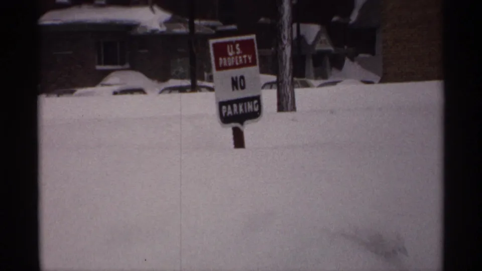1971 Wisconsin 8mm frame with a U.S. Property No Parking sign rising from deep snow beside houses and a partly buried car.