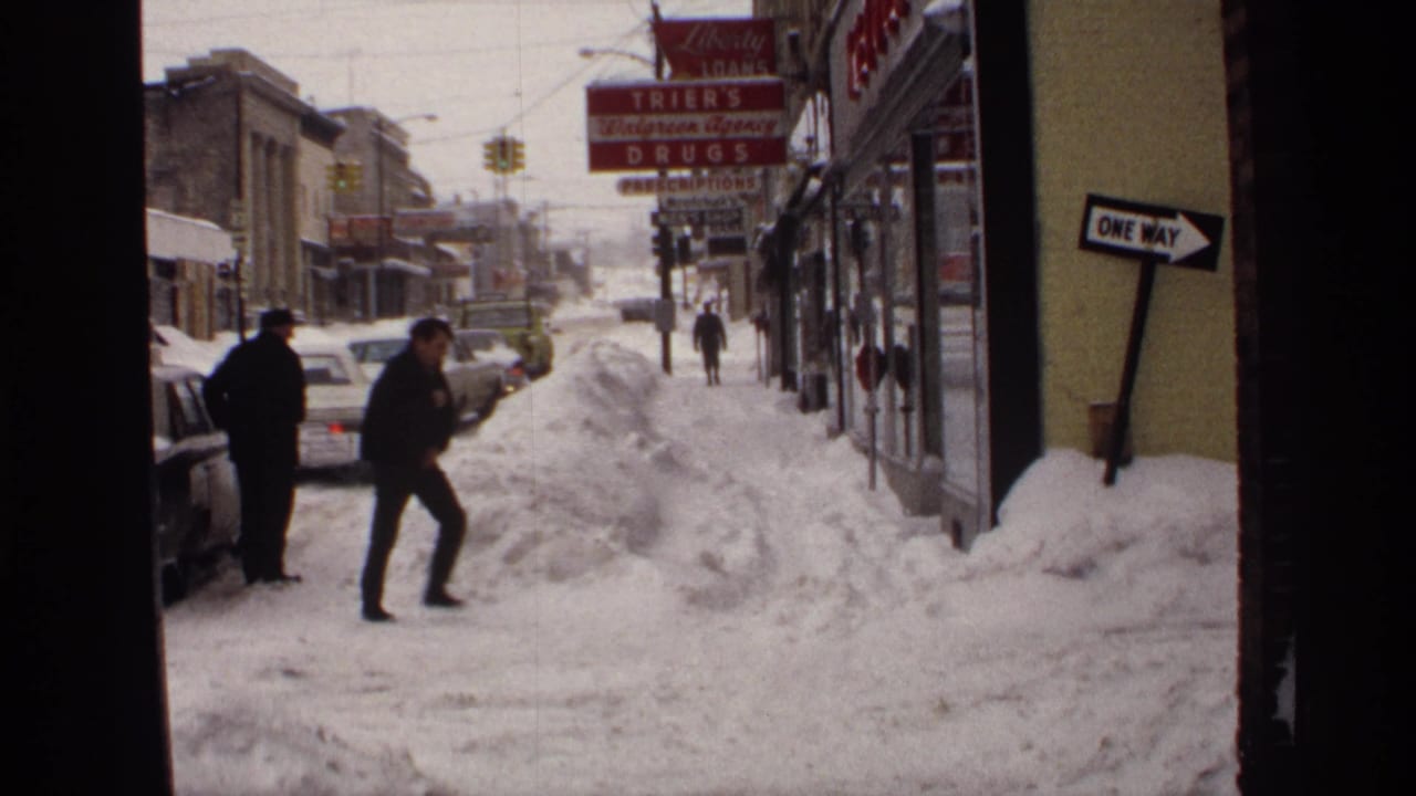 1971 Wisconsin street scene with deep snowbanks, bundled pedestrians, classic parked cars, and a visible drugstore sign.