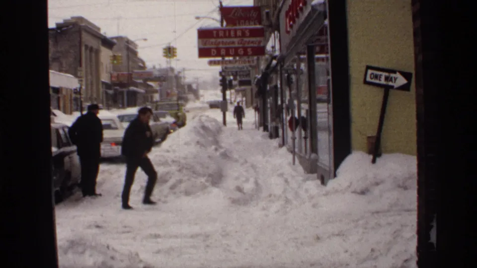 1971 Wisconsin street scene with deep snowbanks, bundled pedestrians, classic parked cars, and a visible drugstore sign.