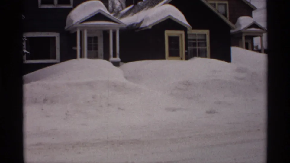 1971 Wisconsin residential view with dark houses partly obscured by high snowbanks after heavy winter snowfall.