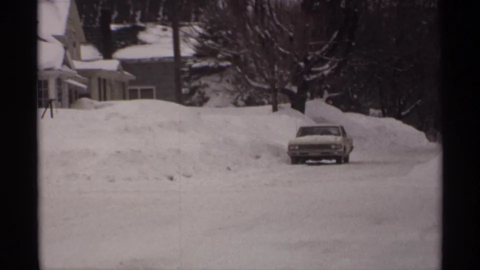 1971 Wisconsin frame showing a classic sedan against tall snowbanks, houses, and winter trees.