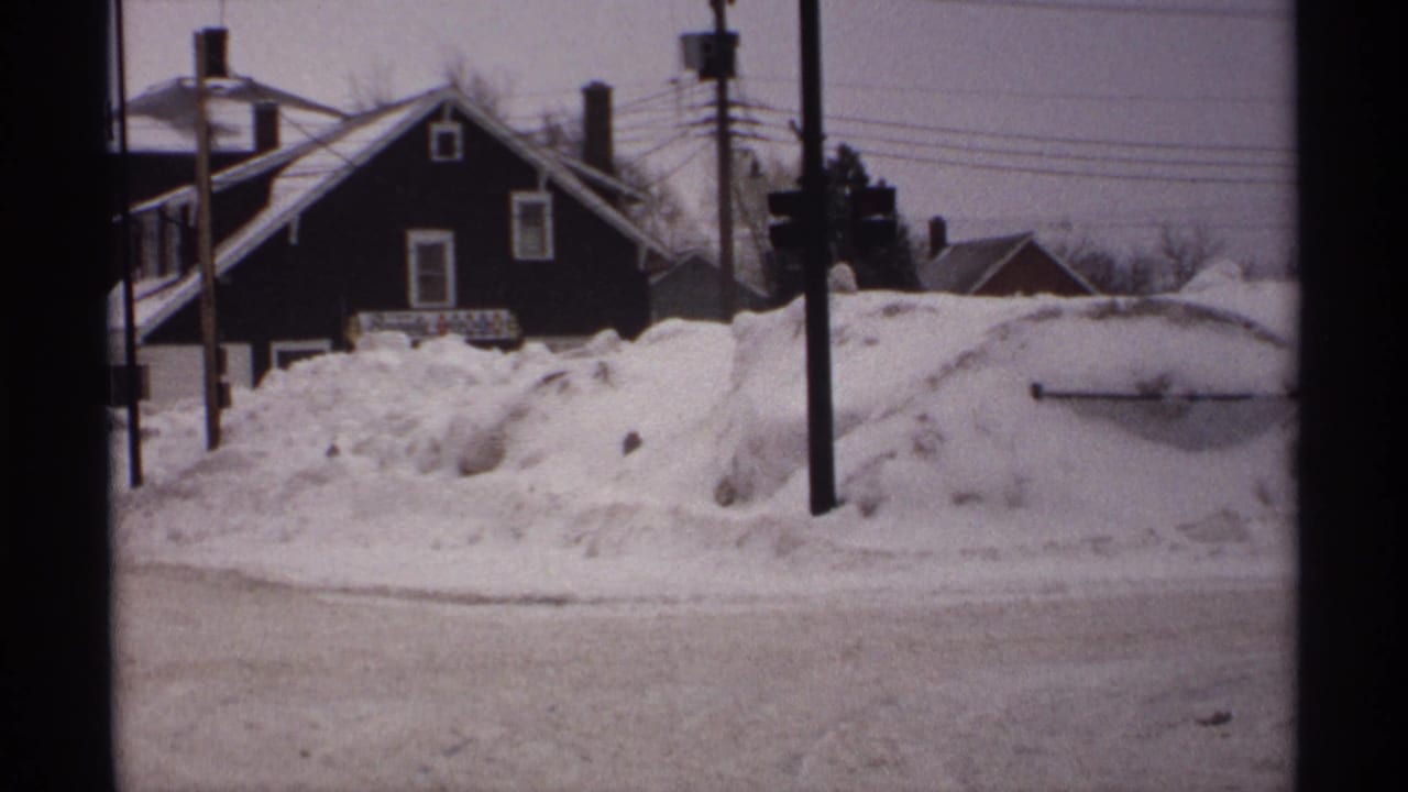 Snowbanks along a quiet street with a dark house, utility poles, and overhead wires.