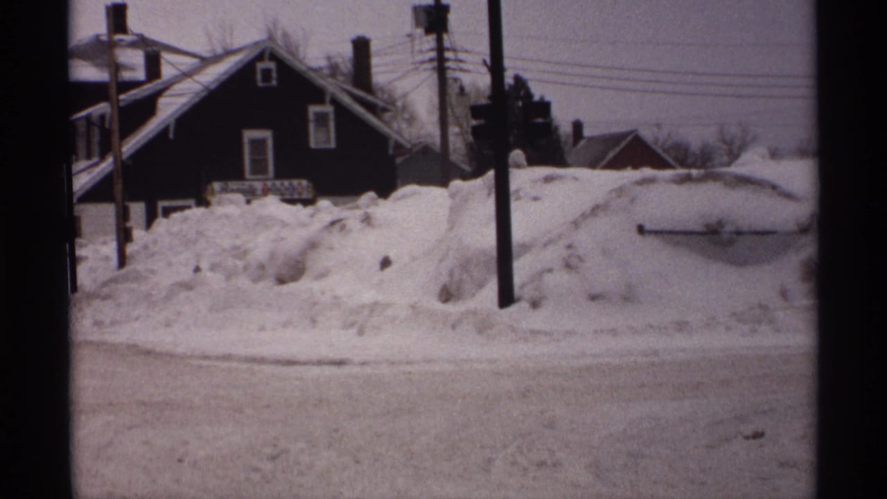 Snowdrifts nearly cover the roadside in front of houses and utility poles.