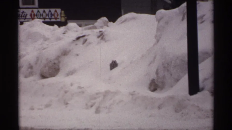 1971 Wisconsin 8mm frame with high roadside snowbanks, a dark pole, and a partially obscured sign that appears to read Beauty Tower.