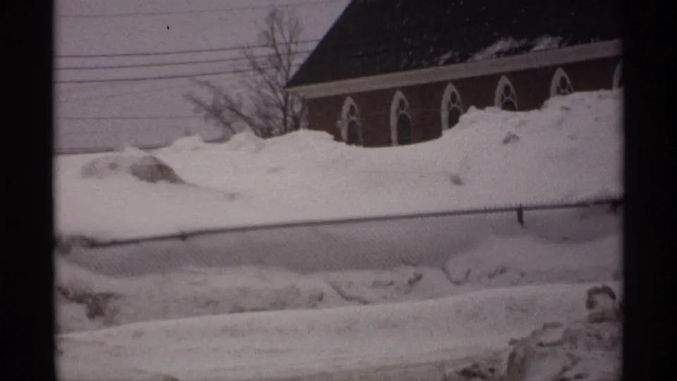 1971 Wisconsin winter frame with a brick church, pointed arched windows, heavy snowbanks, fence, and overhead utility lines.