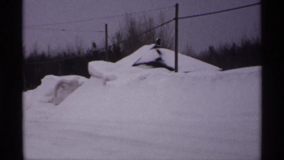 1971 Wisconsin winter roadside view with deep snowdrifts, utility poles, bare trees, and a low snow-covered structure.
