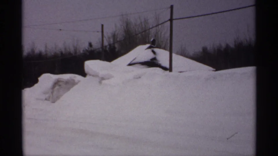 Muted 8mm winter view of a rural Wisconsin roadside with large snowbanks, utility poles, wires, and bare trees under gray sky.