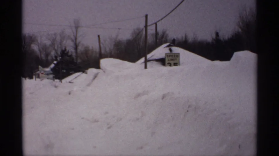 1971 Wisconsin 8mm frame with a SPEED LIMIT 25 sign partly surrounded by tall snowbanks along a rural road.