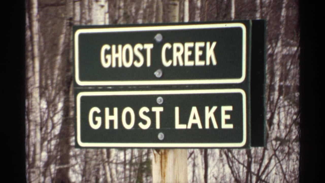 Two green signs reading Ghost Creek and Ghost Lake mounted on a post in snowy woods.