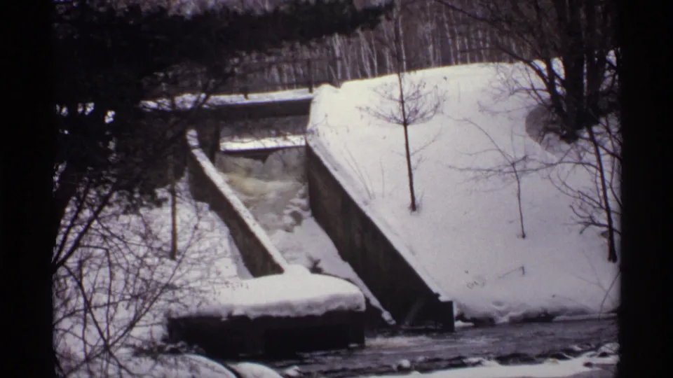 1971 Wisconsin 8mm view of a snow-covered concrete bridge or spillway, bare trees, and dark icy water below.