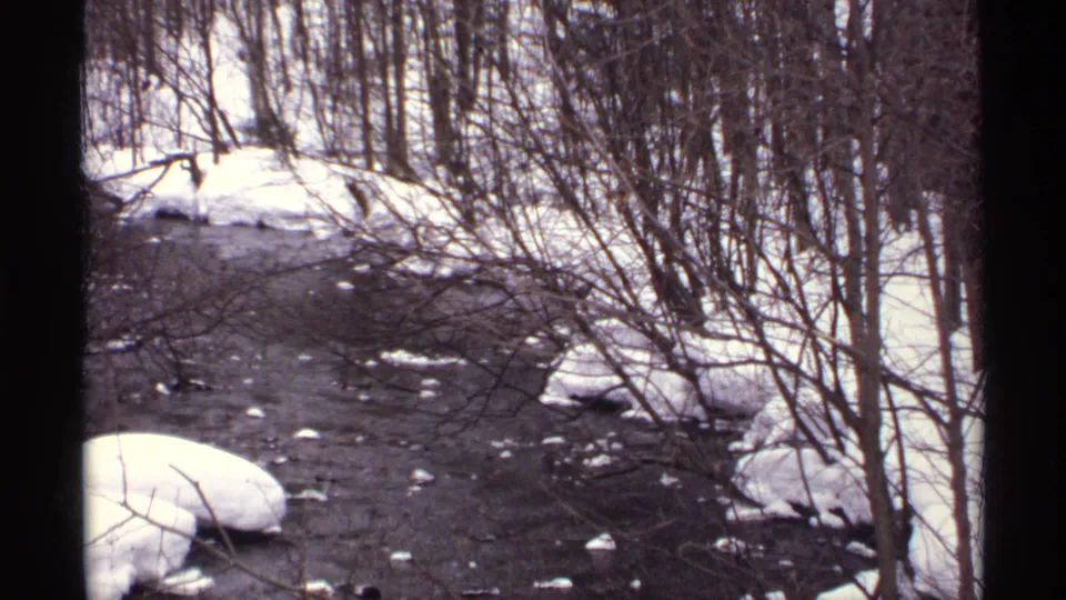 1971 Wisconsin 8mm frame showing a narrow winter river bordered by snow, bare shrubs, and leafless trees.