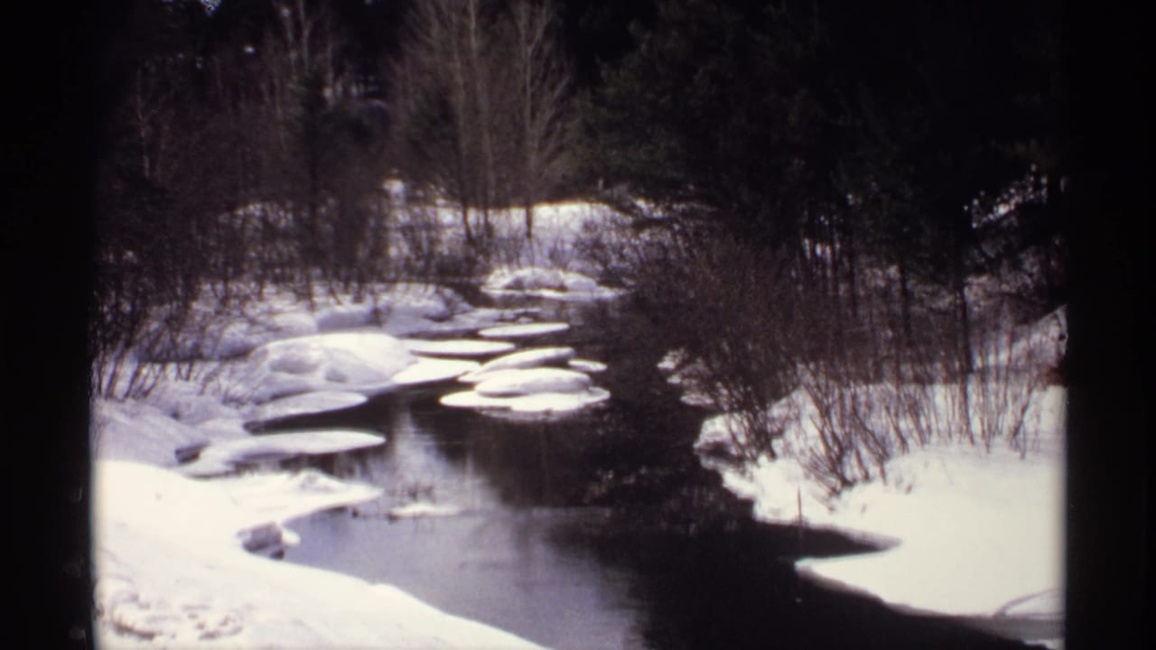 Snowy river bend with flat ice floes and bare winter trees along both banks.