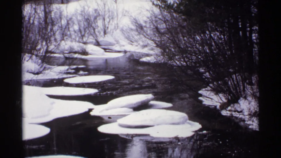 1971 Wisconsin 8mm frame showing clustered white ice floes on a dark river bordered by snowy brush.