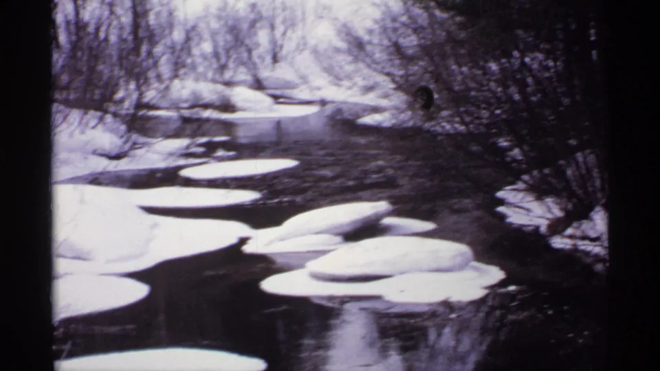1971 Wisconsin home-movie frame with a closer look at white ice sheets drifting or resting on a dark winter river.
