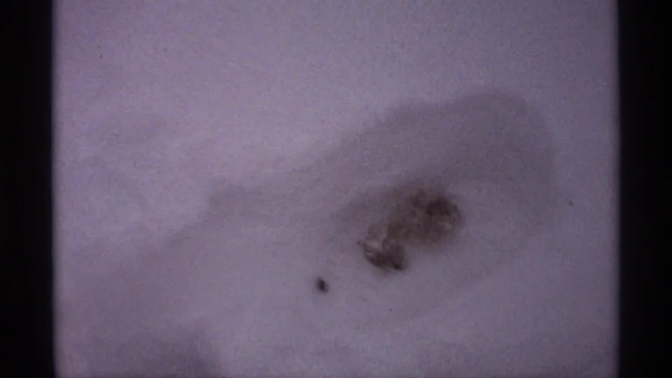 1971 Wisconsin 8mm frame holding on a dark, footprint-like impression in snow, with soft shadowing and scan-edge darkness.