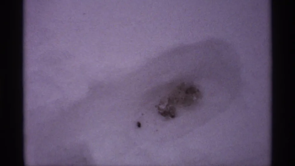 1971 Wisconsin 8mm frame showing a pale snow field or sky-toned snow surface with a small blurred dark patch and visible film edges.