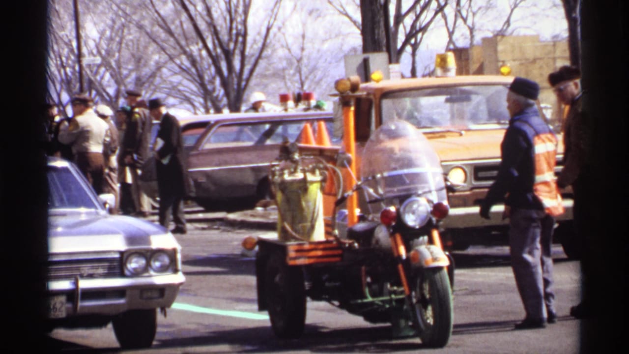 Motorcycle with sidecar equipment parked near yellow trucks and classic cars on a street.
