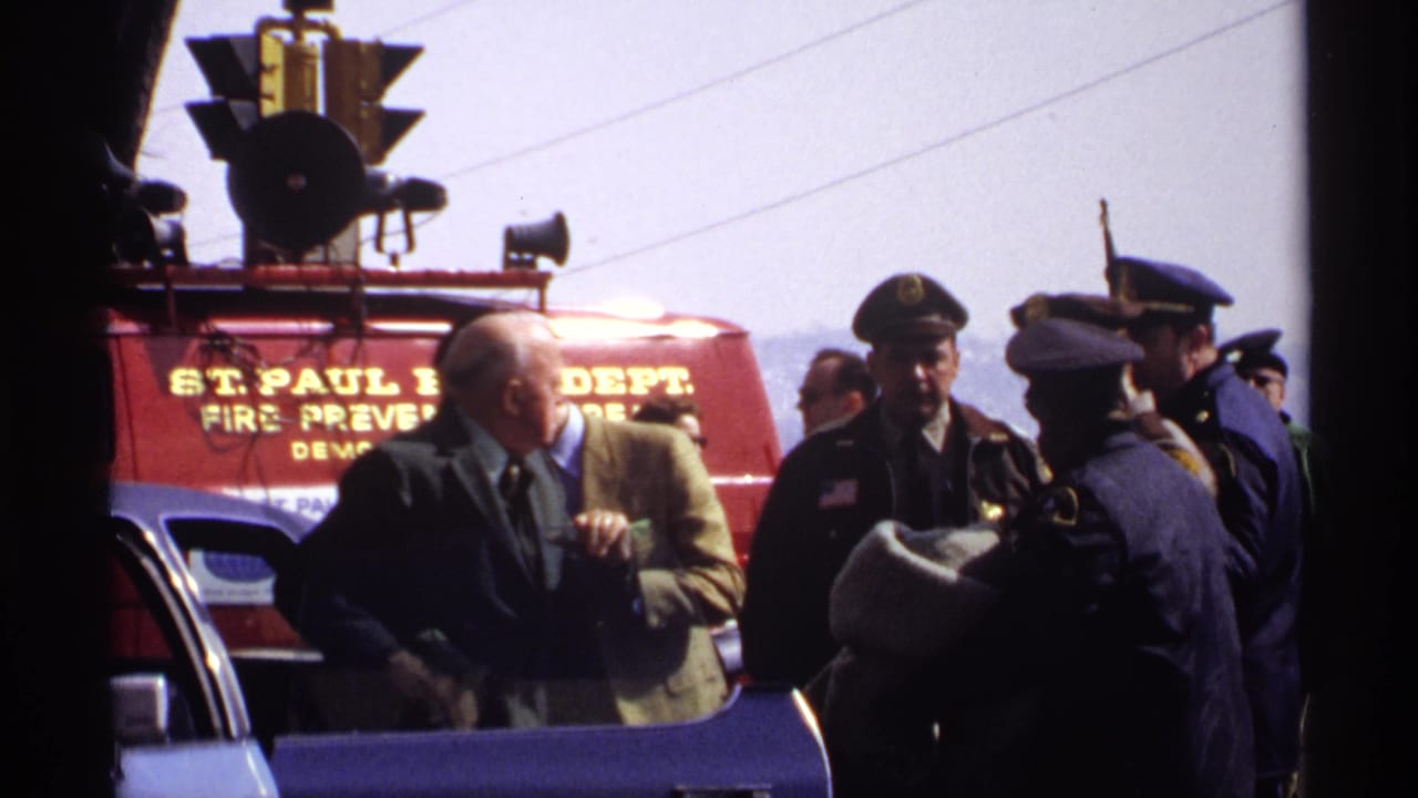 In 1971 home-movie footage associated with Wisconsin, uniformed police officers and men in suits gather beside a red St. Paul Fire Department vehicle during a parade scene.