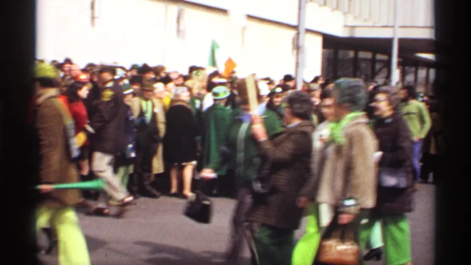 Street-level 1971 Wisconsin parade footage shows marchers in green outfits moving past spectators with signs and Irish-themed accessories.
