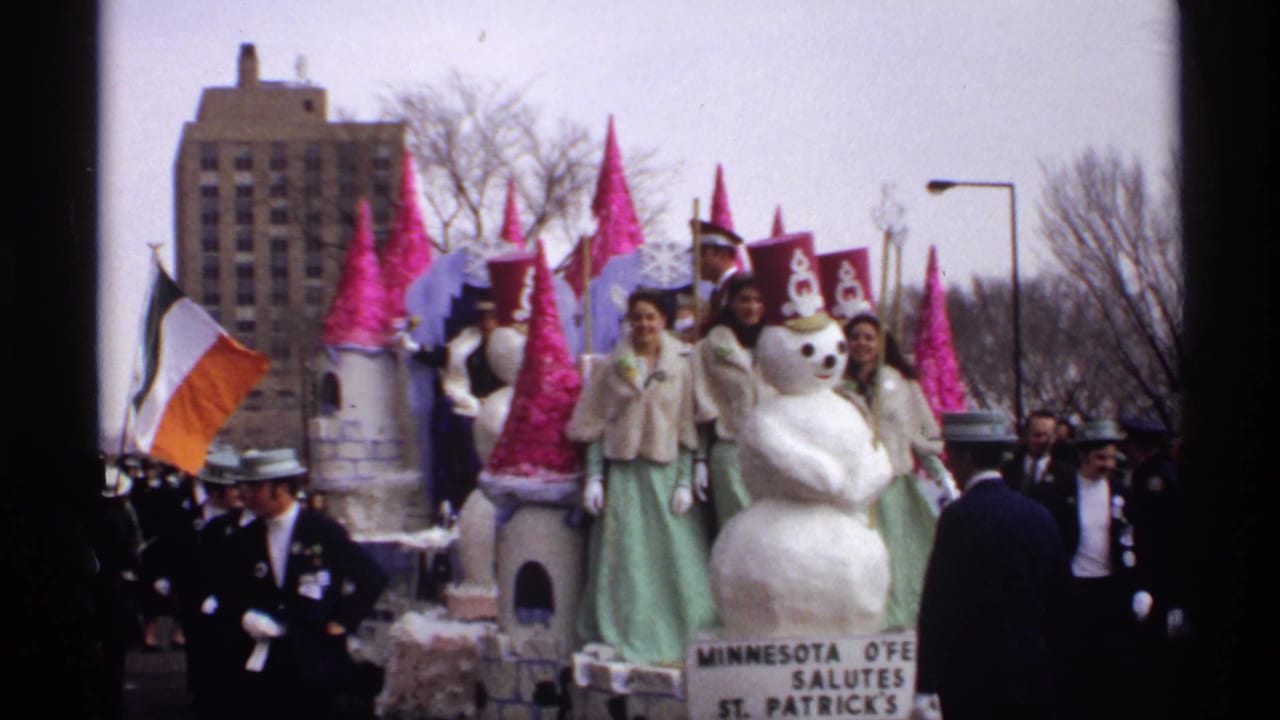 Parade float with snowman figure, pink castle towers, riders, Irish tricolor flag, and uniformed marchers.
