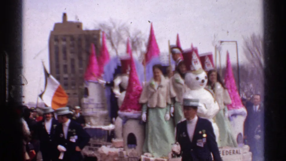 1971 Wisconsin St. Patrick's Day parade scene with the snowman float moving past spectators and a uniformed marcher crossing the foreground.