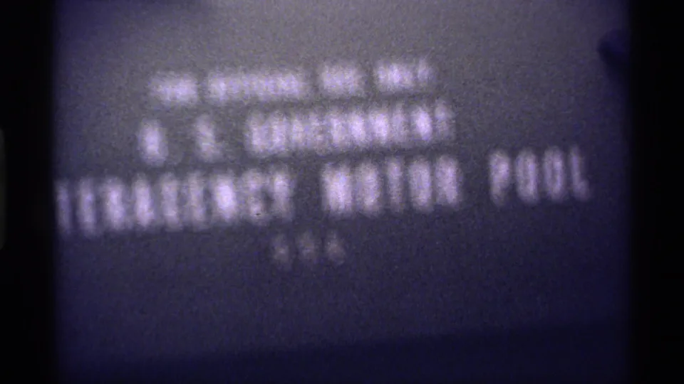 Soft 8mm frame of a filmed U.S. Government Emergency Motor Pool title card, partly blurred and framed by dark film edges.