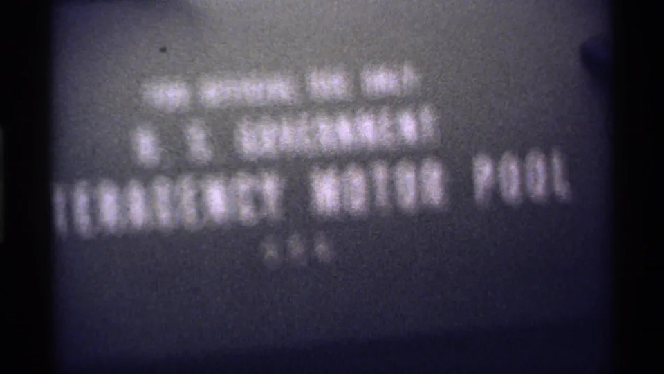 Grainy 8mm title-card frame with soft U.S. Government Emergency Motor Pool lettering and dark gate edges.
