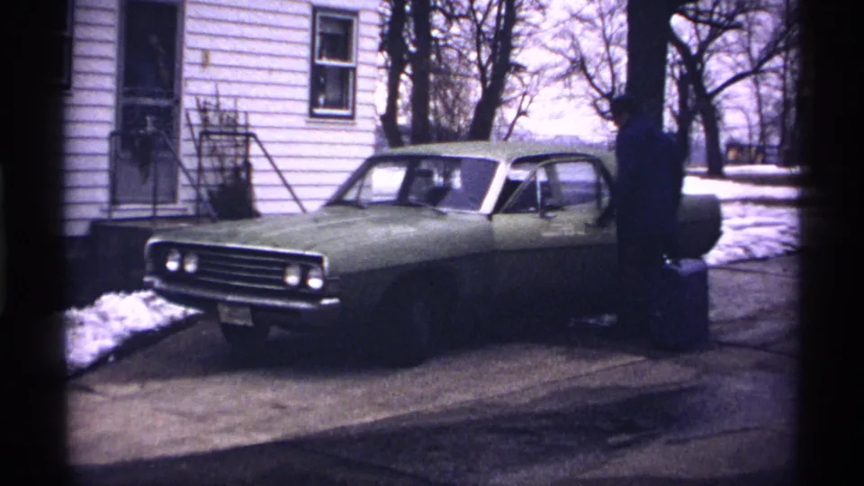 A green two-door car fills the frame while the man stands at the driver's side in a snowy residential Wisconsin setting.