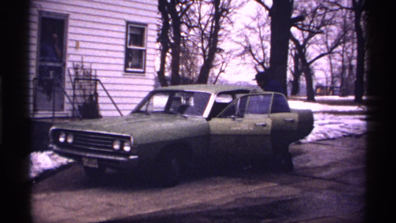 Green sedan parked by a white house with the driver's door open.