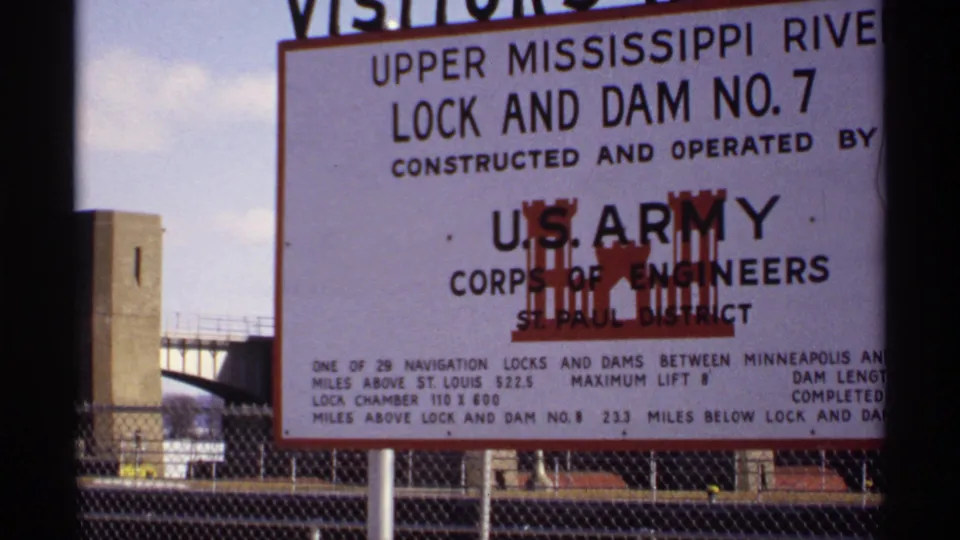 1971 Wisconsin-area view of a U.S. Army Corps of Engineers sign for Upper Mississippi River Lock and Dam No. 7 near fencing and concrete structures.