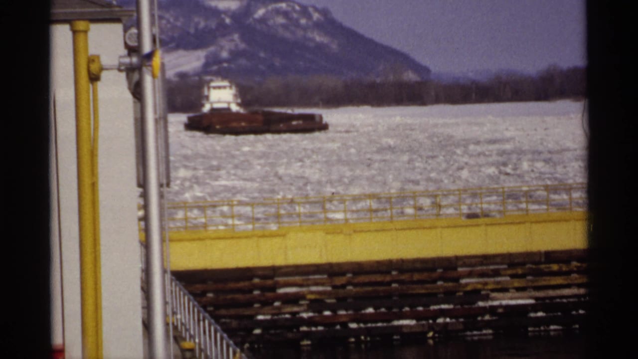 Barge on frozen water with industrial railing and mountain ridge in the background.