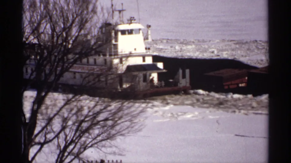 The tugboat appears large in frame as it pushes dark barges through frozen water, with winter trees and snow framing the 1971 Wisconsin scene.