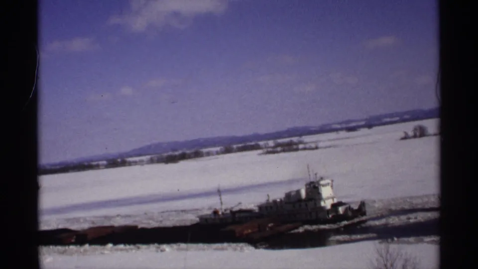 The tugboat and barge pass through the lower frame, with an icy river, snowy banks, and pale clouds behind them.