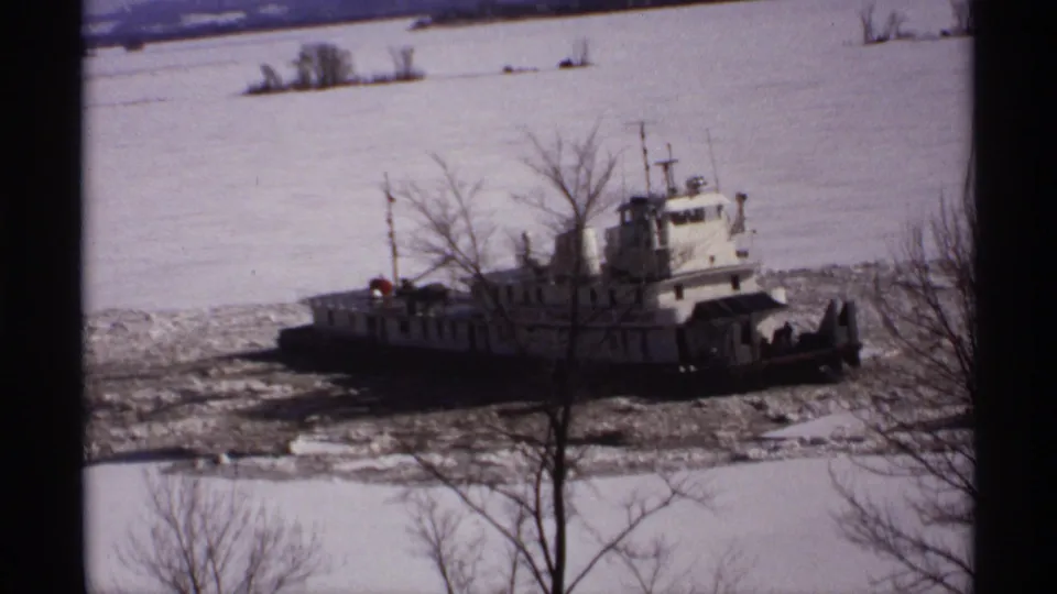 1971 Wisconsin 8mm frame showing a tugboat amid river ice, partly screened by bare winter branches in the foreground.