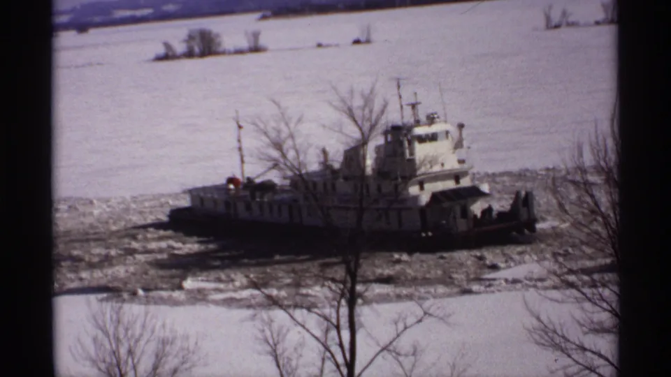 1971 Wisconsin 8mm frame of a tugboat surrounded by broken ice, viewed past winter trees on a snow-covered riverbank.