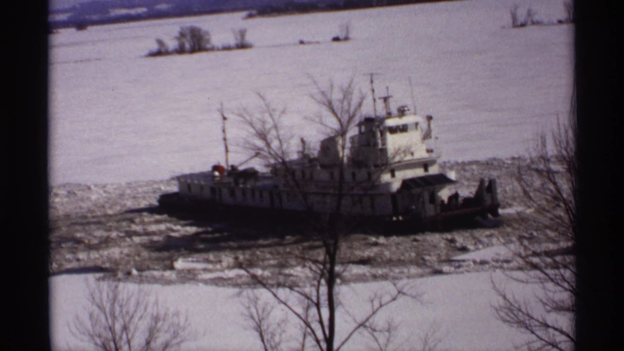 1971 Wisconsin 8mm frame showing a white tugboat in broken river ice, with snow, bare trees, and dark foreground bars.