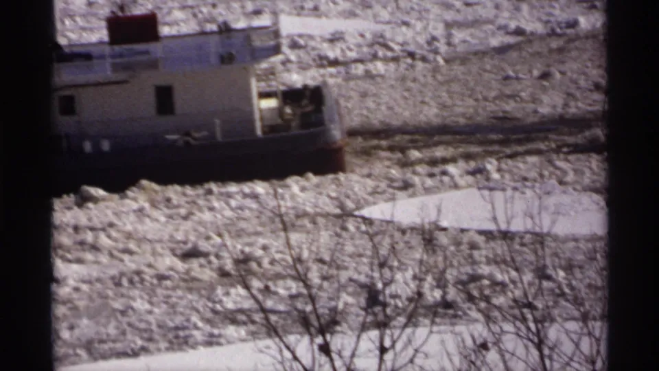 1971 Wisconsin frame showing a closer side view of the tugboat cutting through dense broken ice, with bare branches below.