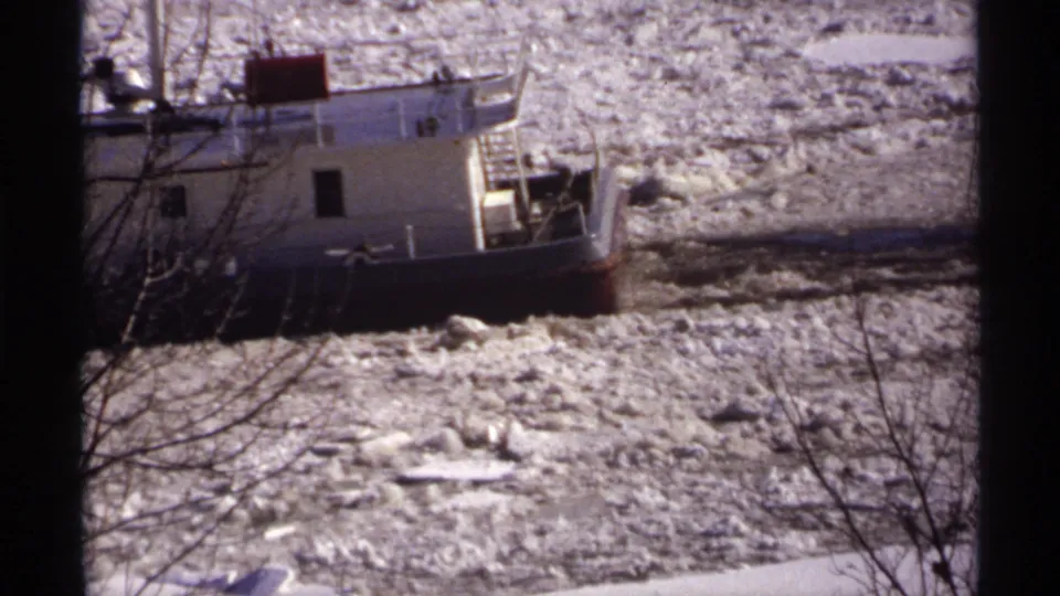 1971 Wisconsin 8mm frame showing the tugboat moving through dense broken ice, partially obscured by leafless foreground branches.