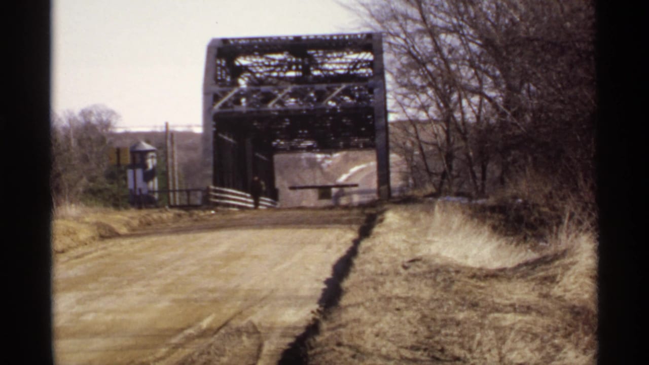Dirt road leading toward a metal truss bridge with a distant person near the entrance.
