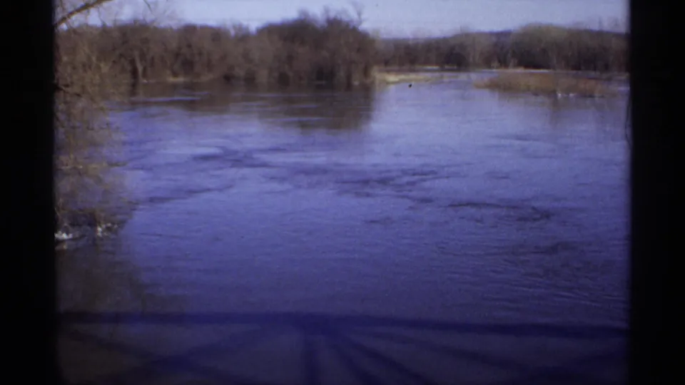 1971 Wisconsin home-movie frame of a wide stream or river bend through a quiet wetland landscape.