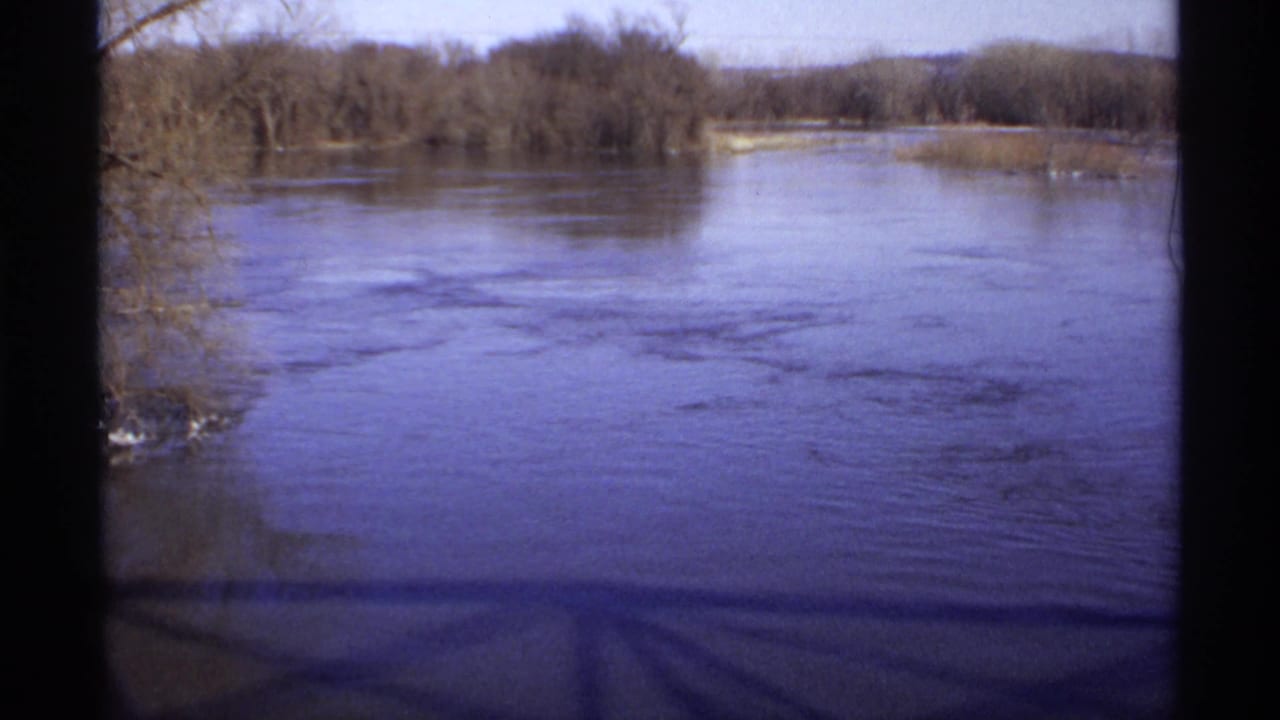 Wide river viewed from a bridge with bare trees along the banks and dark film edges.