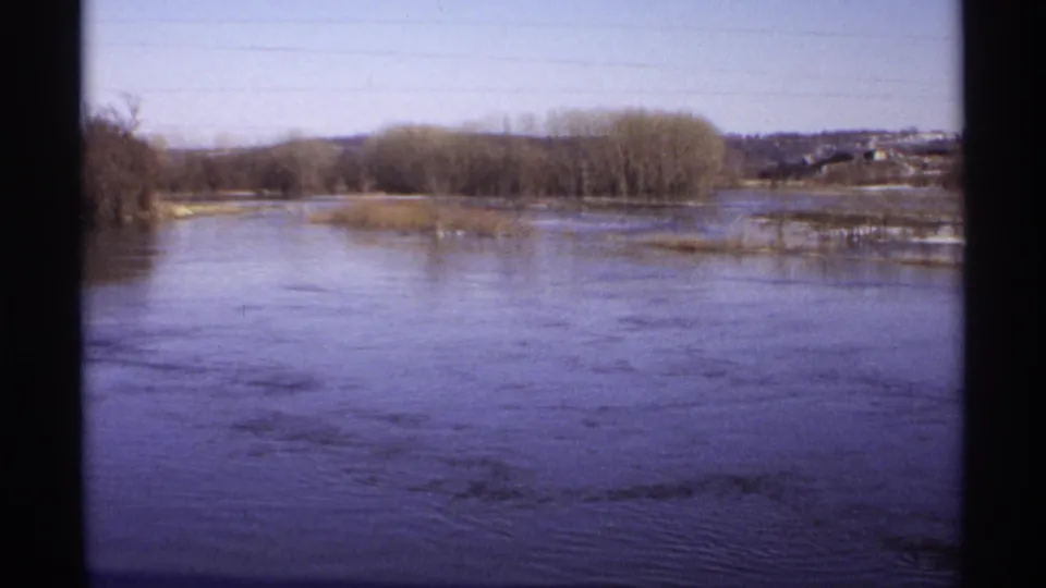 The final frame holds on the broad Wisconsin river landscape, with bare trees, low shoreline, distant structures, and faded 8mm color.