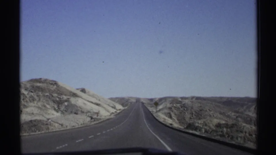 Arizona desert highway seen from a moving vehicle, with low hills and open sky dominating the frame.
