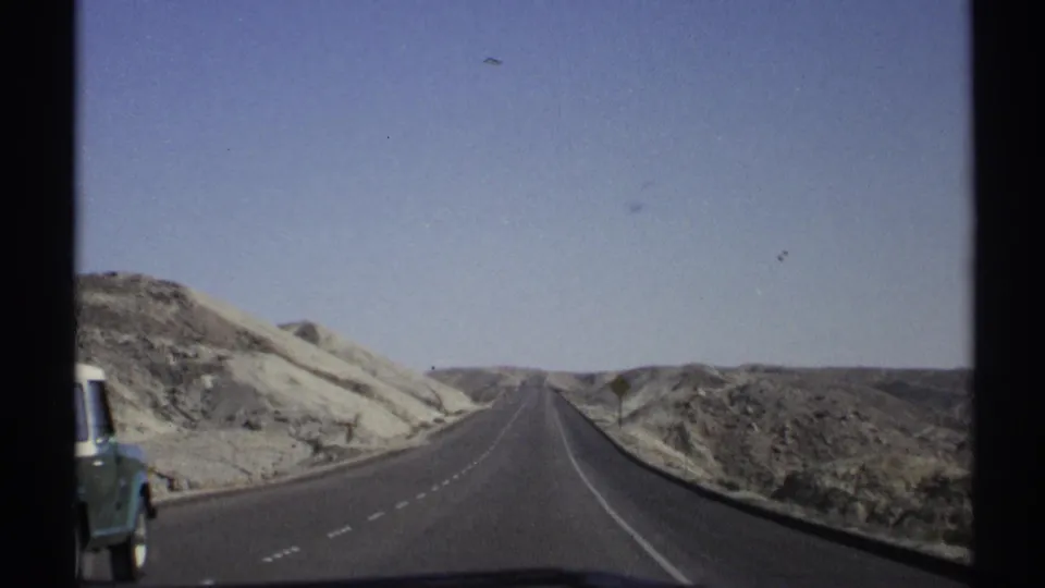 1972 Arizona road scene with a green and white truck passing beside a straight desert highway.