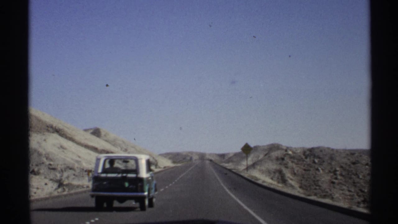 1972 Arizona road-trip footage with a station wagon receding along a desert highway near a roadside warning sign.