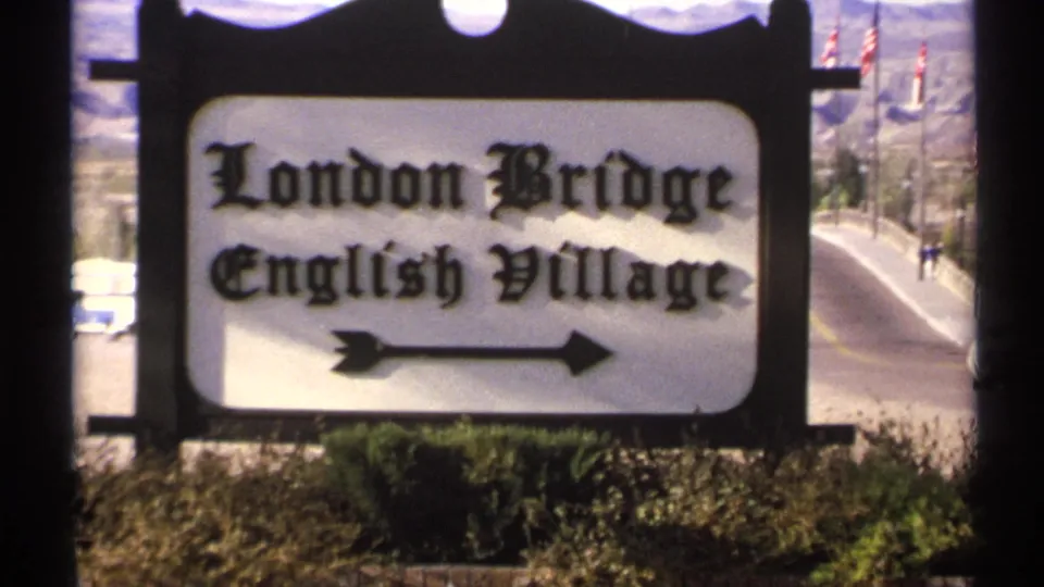 1972 Arizona frame centered on the London Bridge English Village sign, with a road and desert landscape in the background.